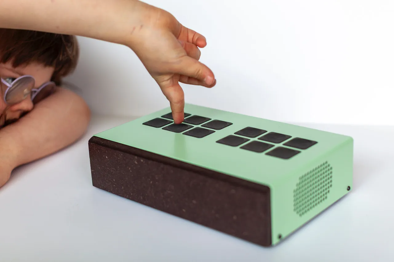 Närbild på ett barn som trycker på knapparna på ett grönt Funki-instrument